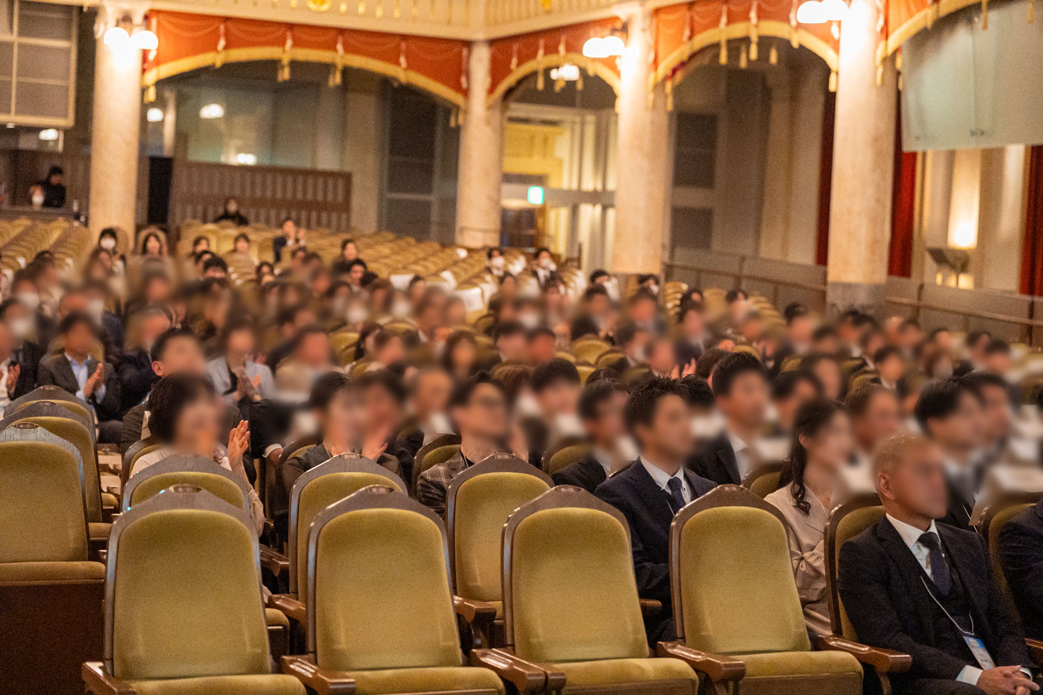 ホールの座席に座って登壇者の話を聞いている数多くの従業員