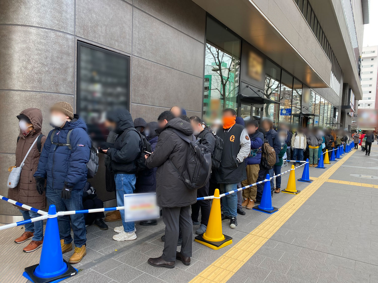 商業施設に入店するために壁沿いに並んで順番待ちをする地域住民